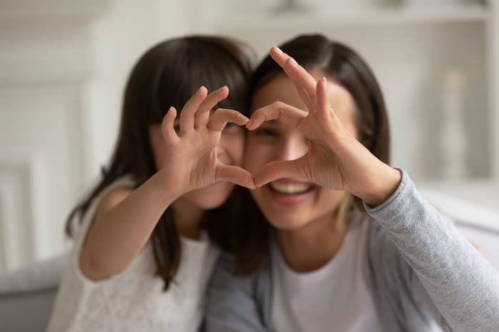 Happy young mother with little daughter making focused heart sign.