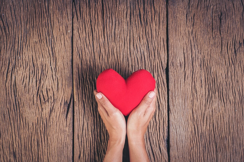 Hand holding red heart on wood background