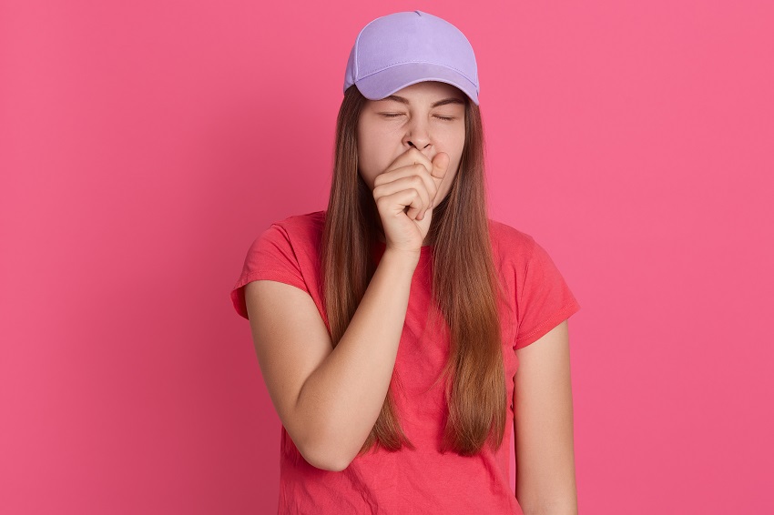 Closeup portrait of tired yawning woman covering her mouth with fist, looks exhausted, wearing t shirt and baseball cap, wants sleep, posing isolated over pink background.