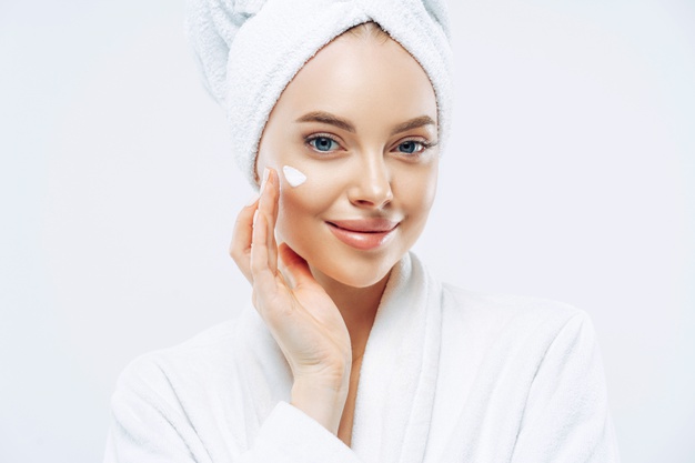 cropped-shot-pretty-young-woman-applies-cream-rejuvenation-healthy-soft-skin-uses-cosmetic-product-demonstrates-nice-effect-body-lotion-wears-comfortable-soft-white-bath-robe-towel_95891-3304