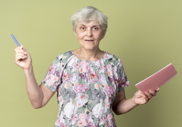 smiling-elderly-woman-holds-notebook-pen-isolated-olive-green-wall_141793-70433